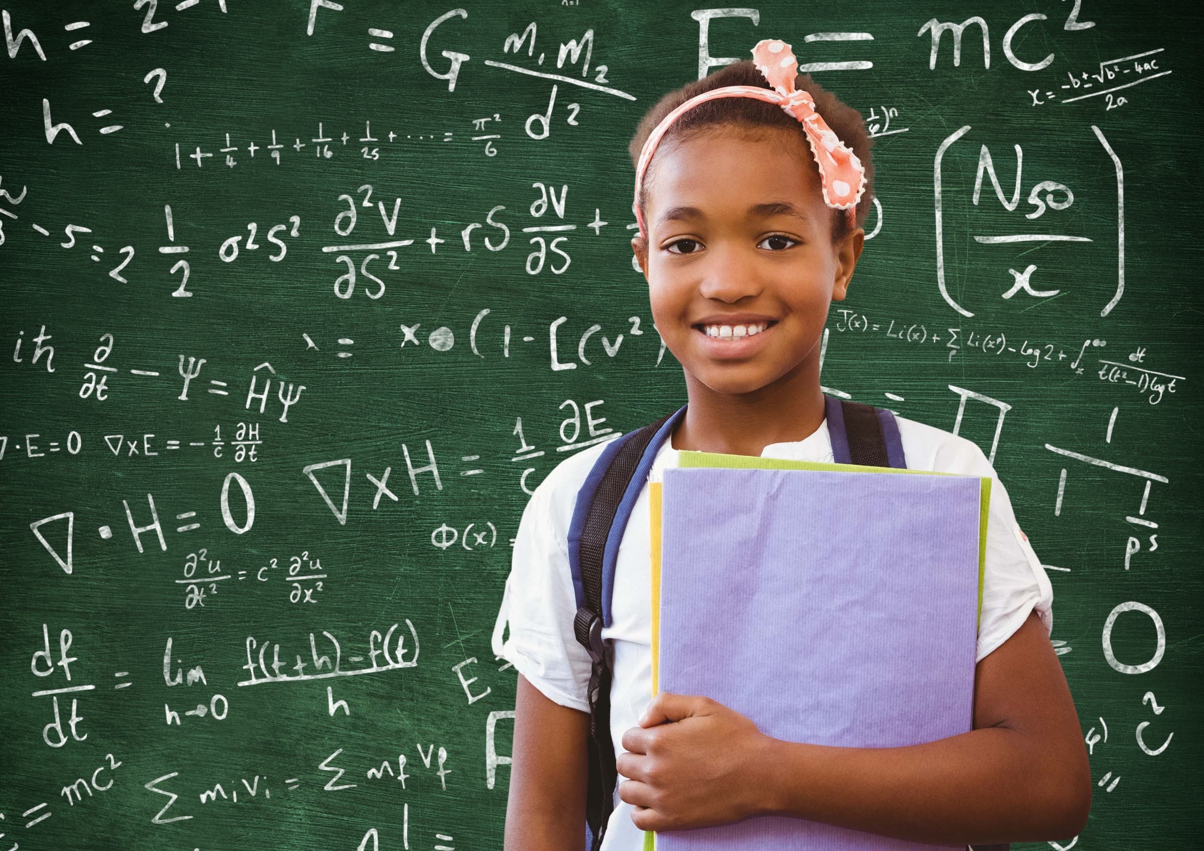 Élève du primaire souriante, ses cahiers dans les bras, devant un tableau couvert de calculs